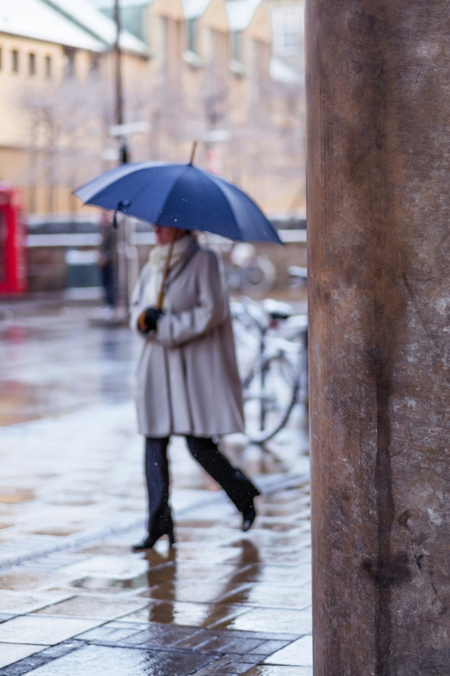 A pedestrian with an umbrella crossing rain-soaked pavement